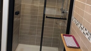 A glass-enclosed shower with a handheld showerhead and a wall-mounted faucet.