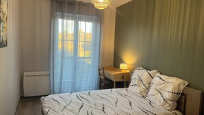 A bedroom with a bed, a desk, a chair, a lamp, and a radiator.