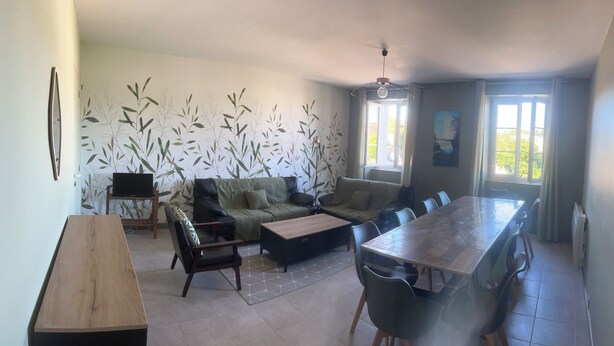 A spacious living area with a sofa set, a dining table with chairs, a wooden coffee table, and a TV on a stand.