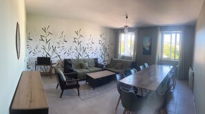 Un vaste espace de vie comprenant un ensemble de canapés, une table à manger avec des chaises, une table basse en bois et un téléviseur posé sur un meuble.