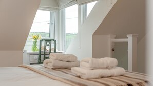 Un dormitorio con cama, toallas, una mesita de noche, una silla y una ventana.