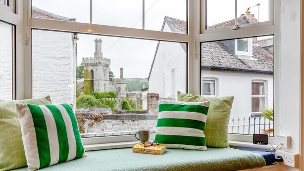 Asiento junto a la ventana con cojines, un libro y una taza.