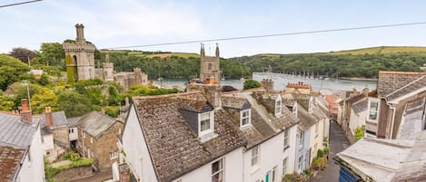 Uma vila costeira com edifícios históricos de pedra, uma igreja imponente e um rio com barcos.