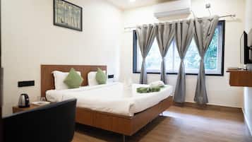 A hotel room with a bed, a desk, a chair, a window with curtains, an air conditioning unit, and a wall-mounted television.