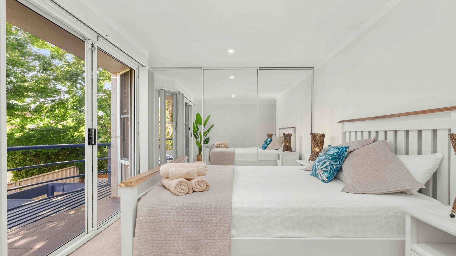 A modern bedroom with a large bed, a balcony, and a sliding glass door leading to an outdoor area.