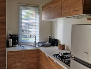 A modern kitchen with wooden cabinets, a stainless steel sink, a coffee maker, a toaster, and a Cobalt refrigerator. - Cozy mobile home for 2 with equipped kitchen (Pordic)