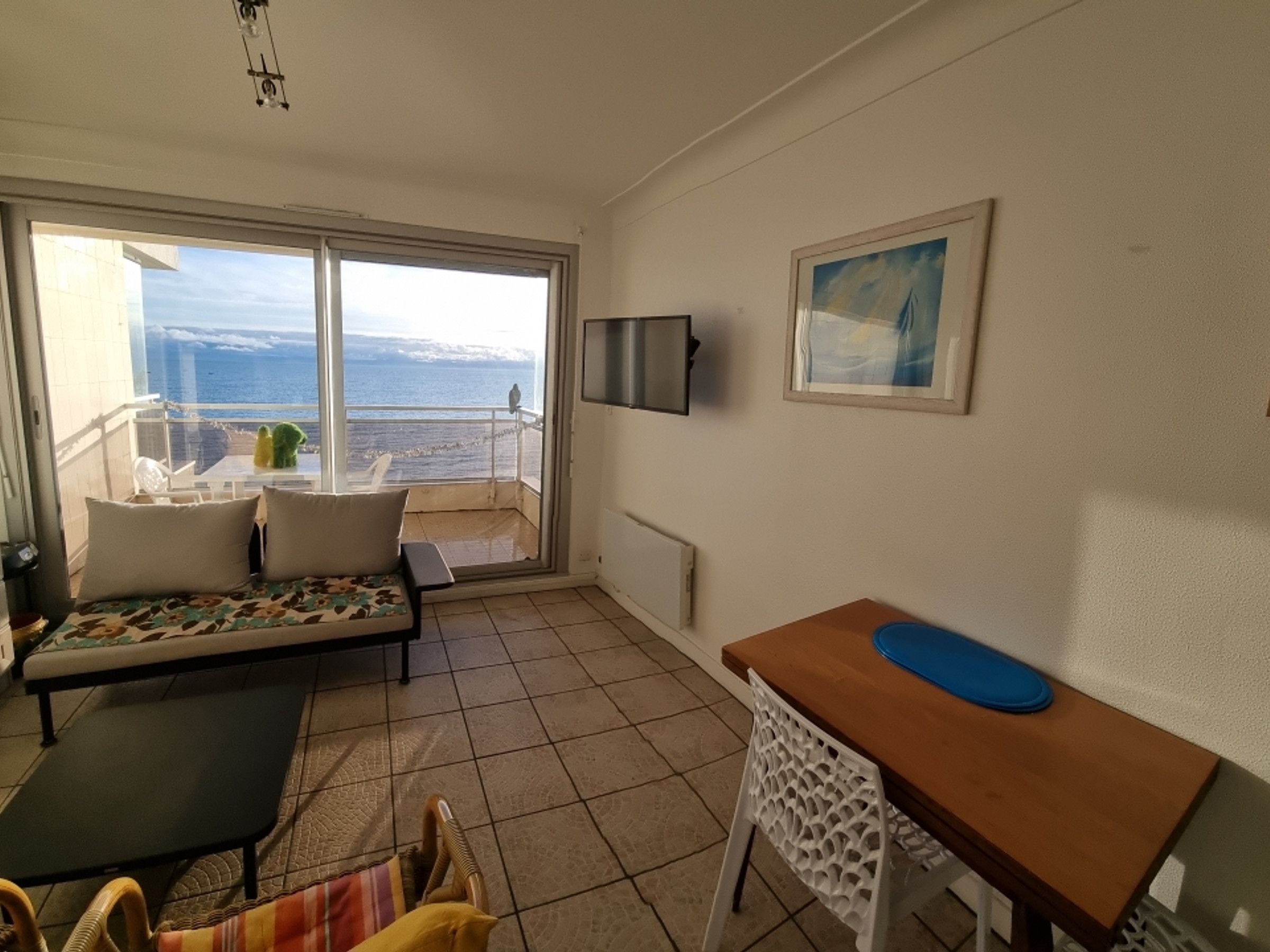 Een balkon met uitzicht op zee en bergen, een bank, een tafel en een stoel.