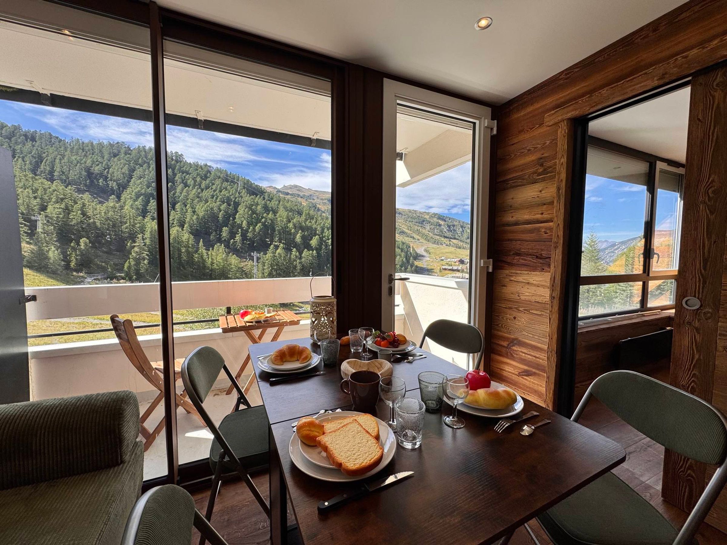 A dining area with a table set for two, overlooking a mountainous landscape through large windows.