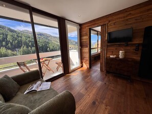 Uma sala de estar moderna com uma janela ampla, piso de madeira e uma TV de tela plana presa à parede.