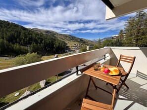 Varanda com mesa e cadeiras de madeira, com vista para uma paisagem montanhosa e céu limpo.