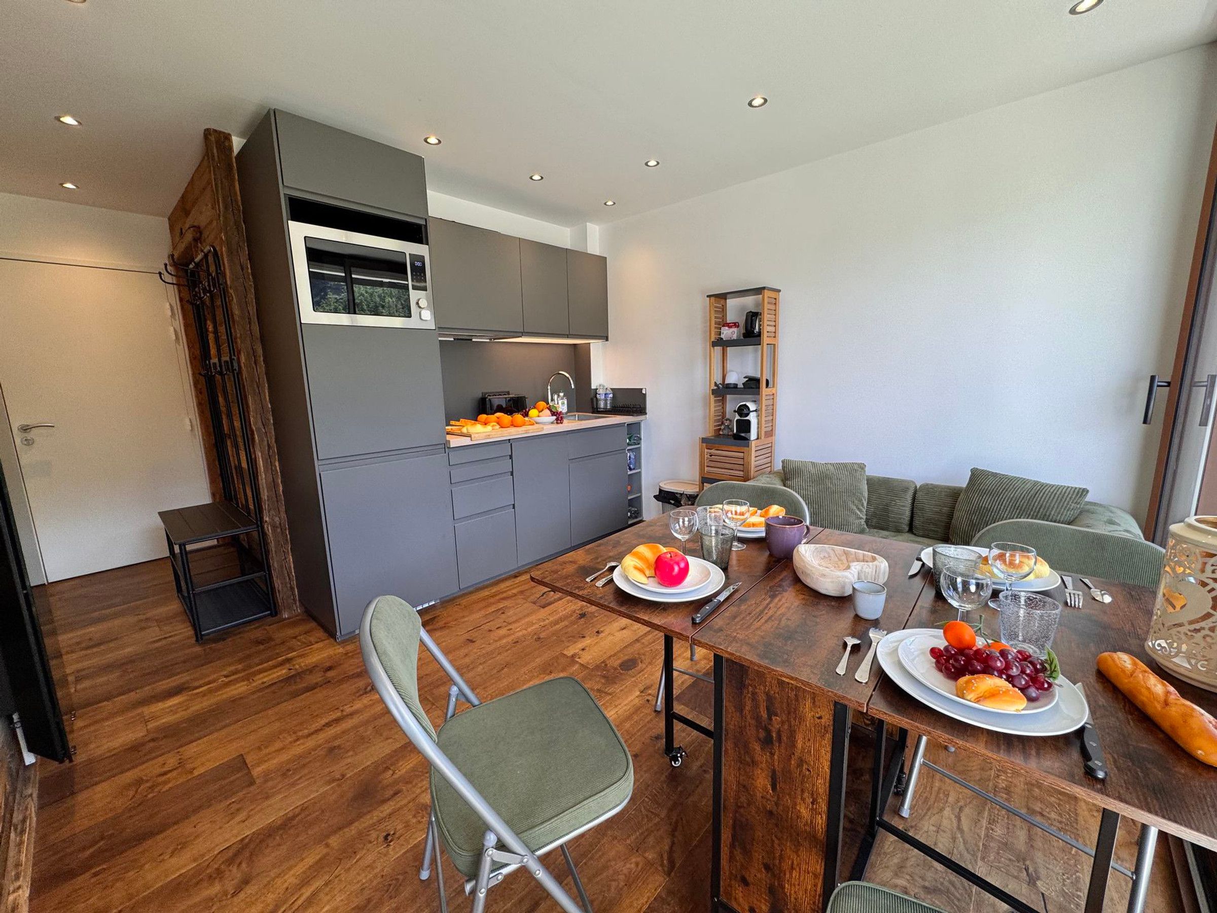 A modern kitchen with grey cabinets, a wooden dining table set with plates, glasses, and cutlery.