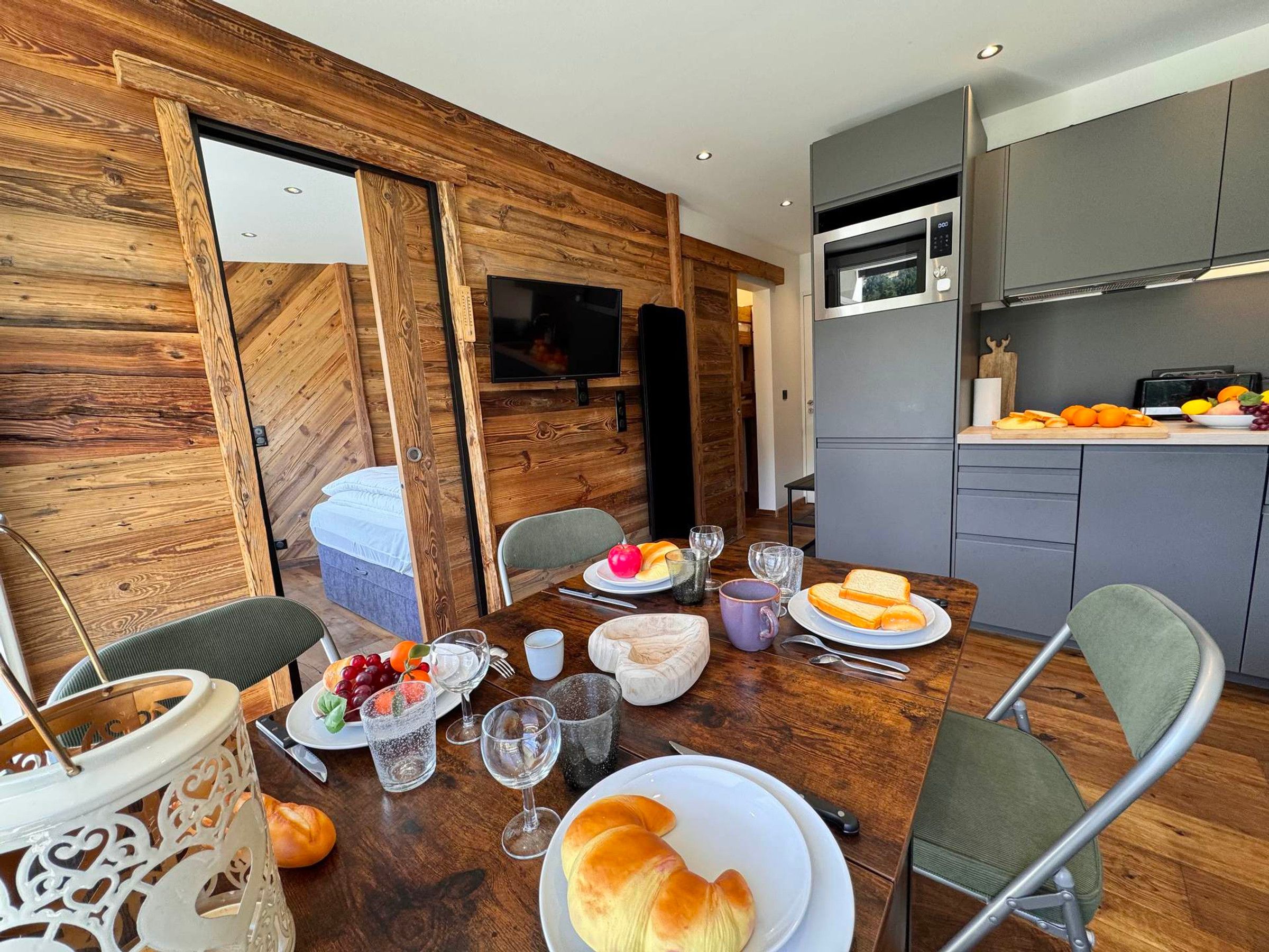 Uma área de refeições acolhedora com uma mesa de madeira posta para uma refeição, uma cozinha com eletrodomésticos modernos e uma porta de correr que dá para outro cômodo.