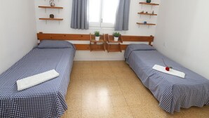 Ein kleines, sauberes Zimmer mit zwei Einzelbetten, Holz-Kopfteilen und Regalen mit Dekoration.