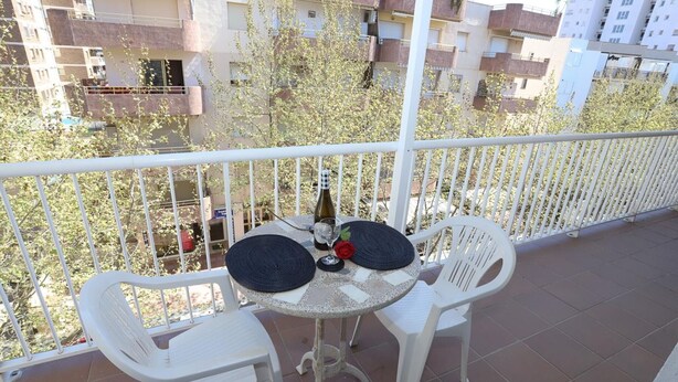 Ein Balkon mit zwei weißen Plastikstühlen und einem kleinen runden Tisch, einer Flasche und einem Glas.