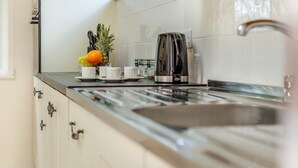 A kitchen with white cabinets, a stainless steel sink, a coffee maker, and a fruit bowl with an orange and pineapple. - 2 Bed in Looe (oc-g32529) (Looe)