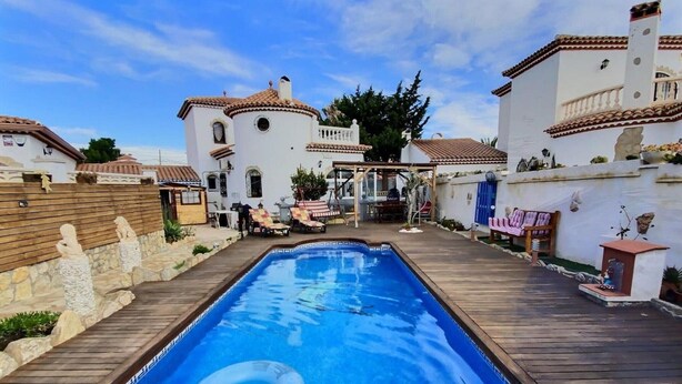 A swimming pool with a wooden deck, surrounded by white buildings with red-tiled roofs. - Charming Two-Story Villa with Private Pool and Garden in Miami Platja, Close to Catalan Coast (Miami Playa)