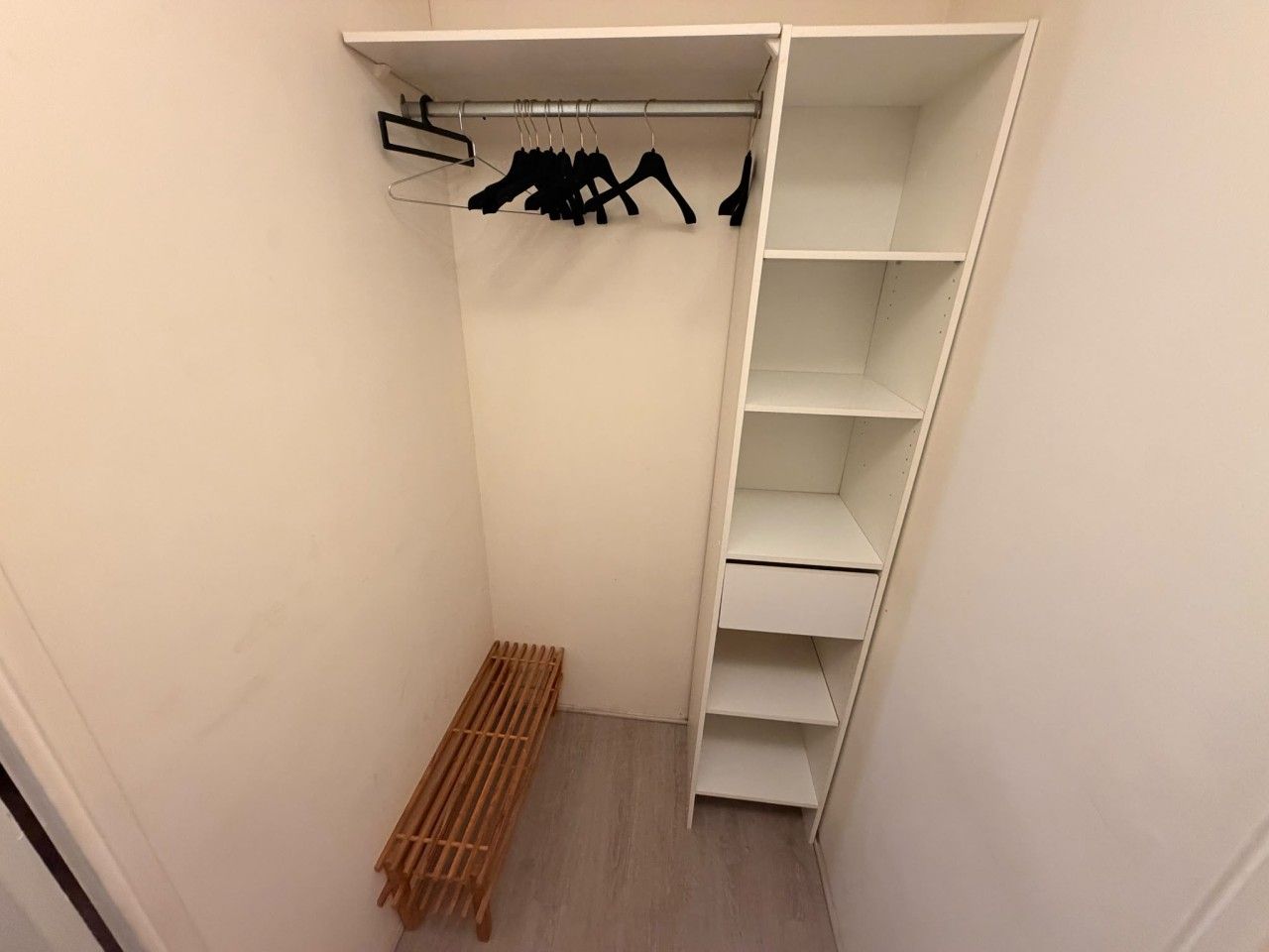 A walk-in closet with a wooden bench, a clothing rack with hangers, and multiple shelves.
