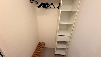 A walk-in closet with a wooden bench, a clothing rack with hangers, and multiple shelves.