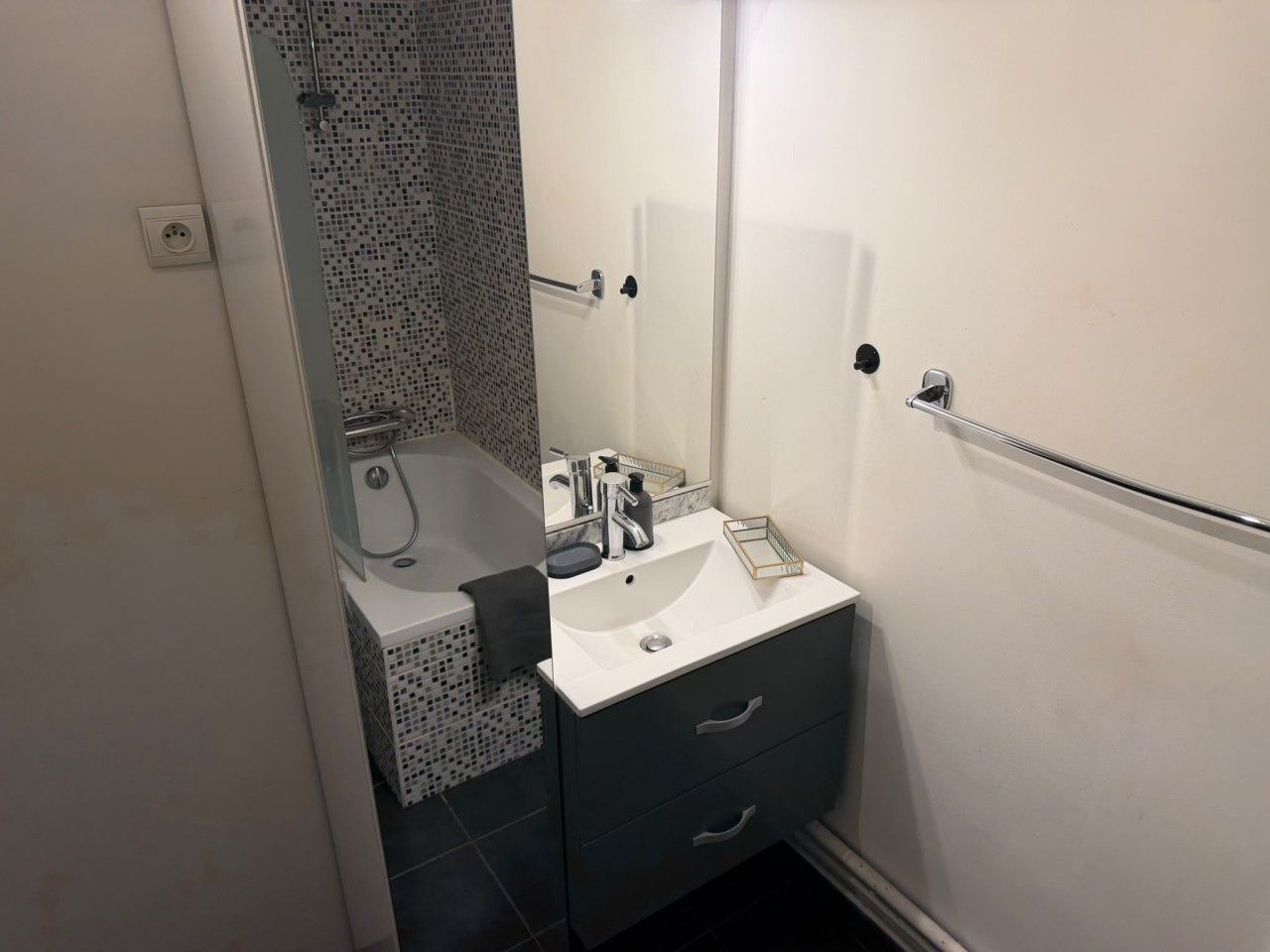Een badkamer met een witte wastafel, een kastje in donkere tinten en een douchecabine met glazen wanden.
