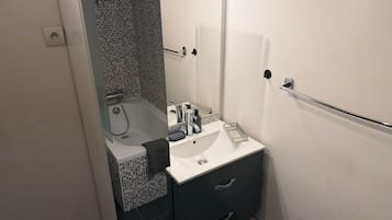 Een badkamer met een witte wastafel, een kastje in donkere tinten en een douchecabine met glazen wanden.
