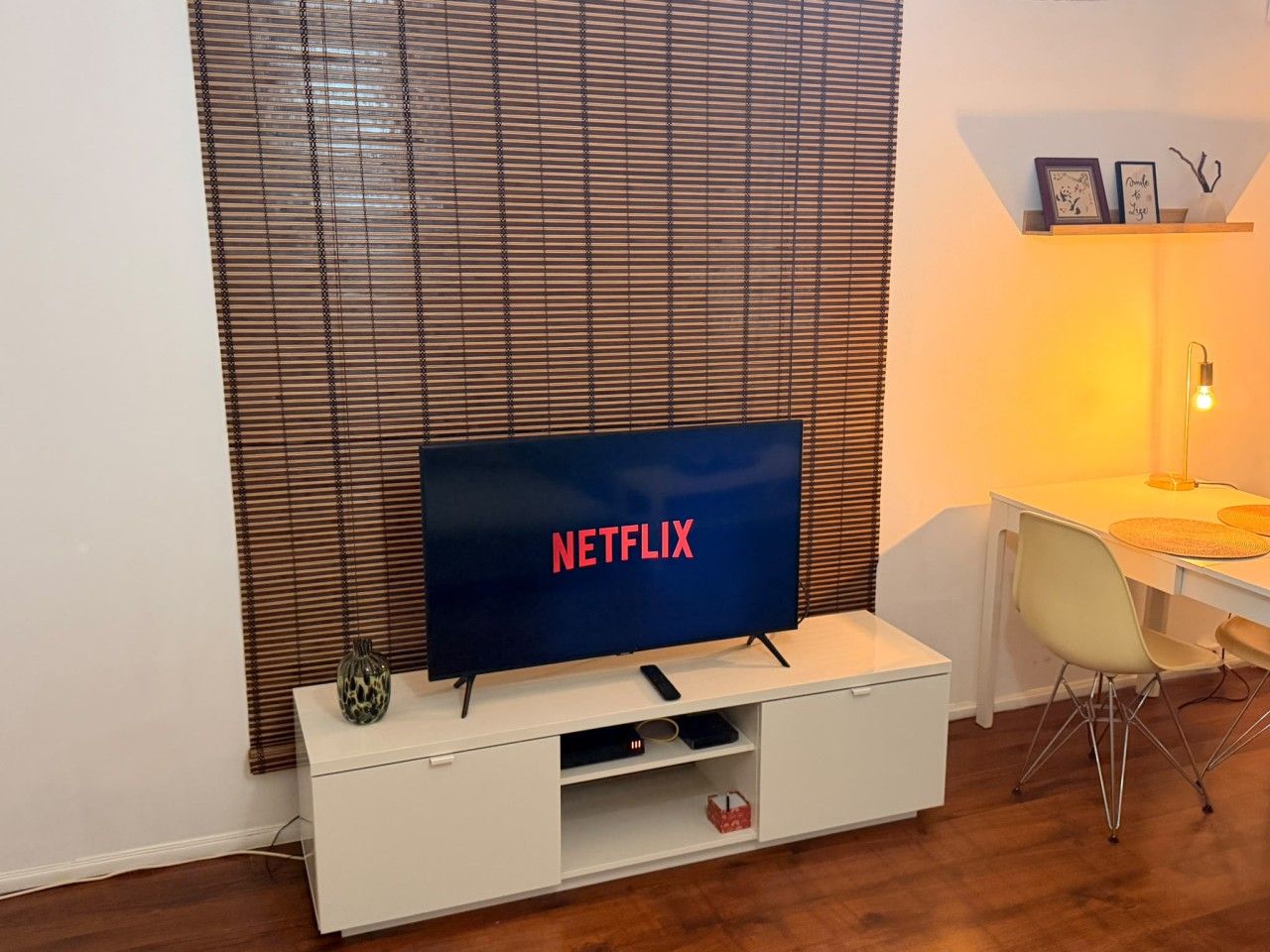 Une pièce avec un téléviseur affichant le logo de Netflix, un bureau blanc, une chaise et une lampe.