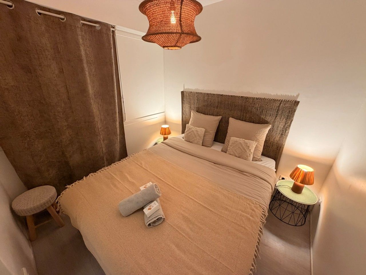 A neatly made bed with a headboard, a bedside lamp, and a rolled towel on the bed.