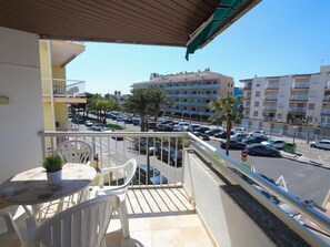Un balcon avec une table et des chaises, donnant sur un parking et des immeubles.