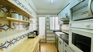 A kitchen with patterned tiles, wooden shelves, a built-in oven, and a window. - Spacious Apartment 300m from Salou Beach with A/C and Terrace (Salou)
