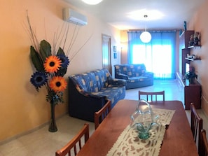 Una sala de estar con un sofá, una mesa de comedor con sillas, un florero con flores y un ventilador de techo.