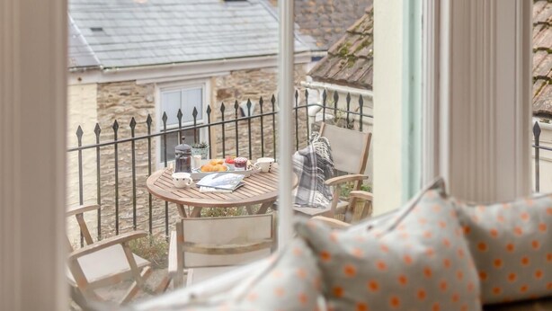 En hyggelig balkon med et rundt træbord dækket til morgenmad, med croissanter, kaffe og en bog.
