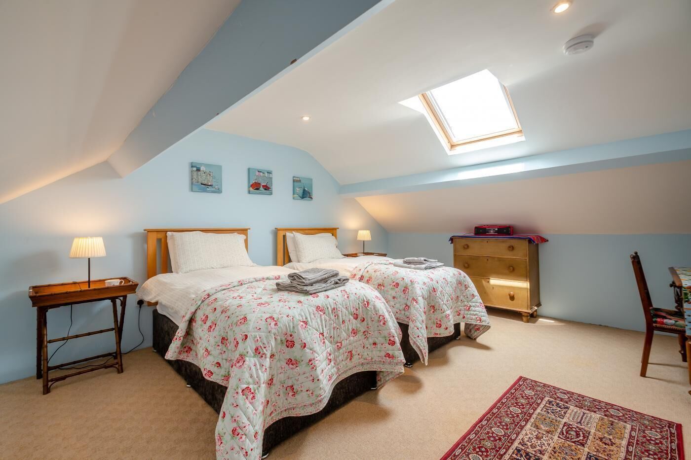A cozy attic bedroom with two beds, a skylight, a wooden dresser, and a small desk.