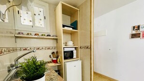 Una cocina compacta con encimera de granito, un refrigerador blanco, un microondas y una planta en maceta.