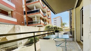 Un balcón con una mesa de vidrio y dos sillas, una planta en maceta y vistas a edificios cercanos.