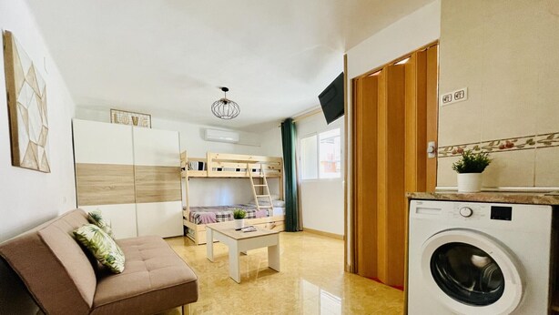 Un espacio habitable pequeño con sofá, literas, lavadora y una mesita.