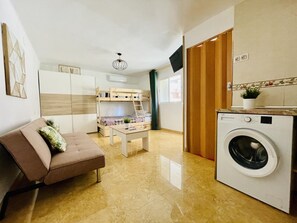 Un espace de vie compact comprenant un canapé, des lits superposés, un lave-linge et une petite table.