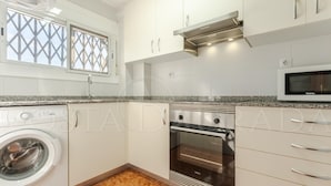 Eine moderne Küche mit Einbauwaschmaschine, Backofen, Mikrowelle und einem Fenster mit dekorativem Sichtschutz.