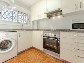Una cocina moderna con lavadora integrada, horno, microondas y una ventana con celosía decorativa.