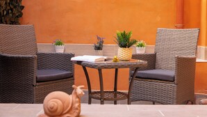 A wicker outdoor seating area with two chairs, a small table, and potted plants. - Rental in Rome Gregoriana Apartment (Rome)