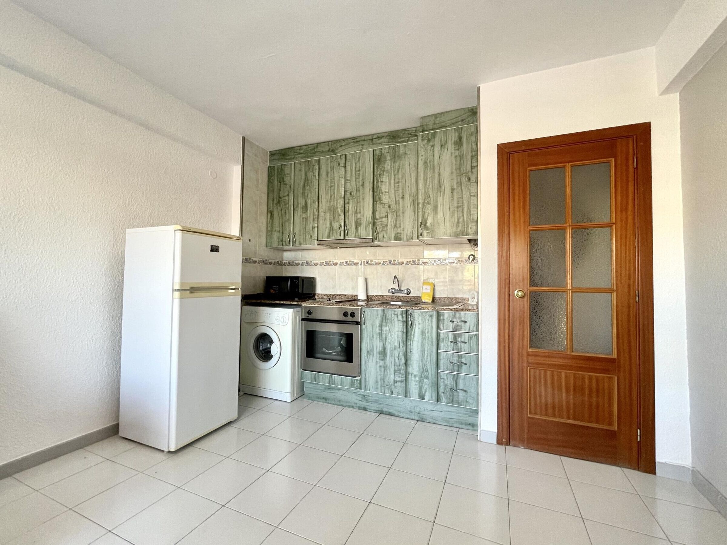 A compact kitchen with a refrigerator, washing machine, oven, and microwave.