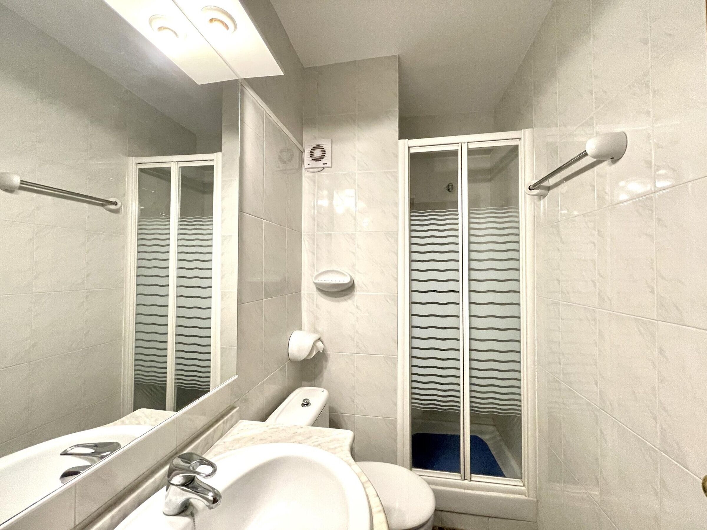 A bathroom with a sink, mirror, towel dispenser, and a shower with a striped curtain.