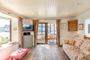 A cozy room with a television, a sofa, a dining table with chairs, and a view of the outdoors.