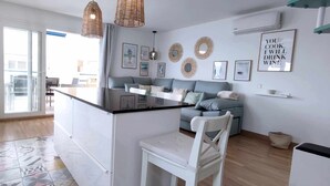 A modern kitchen with a dining area, featuring a white countertop, a dining table, and a sofa. There are decorative wall mirrors and a framed quote on the wall. - Albaida Gardens (El Morche)