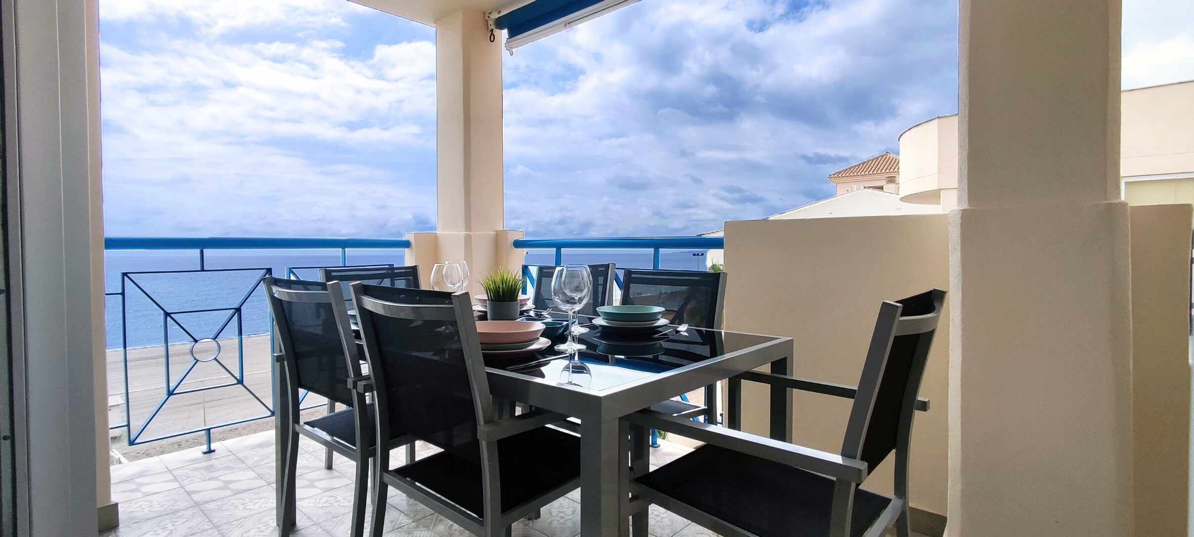 A balcony with a table set for dining, overlooking the sea.