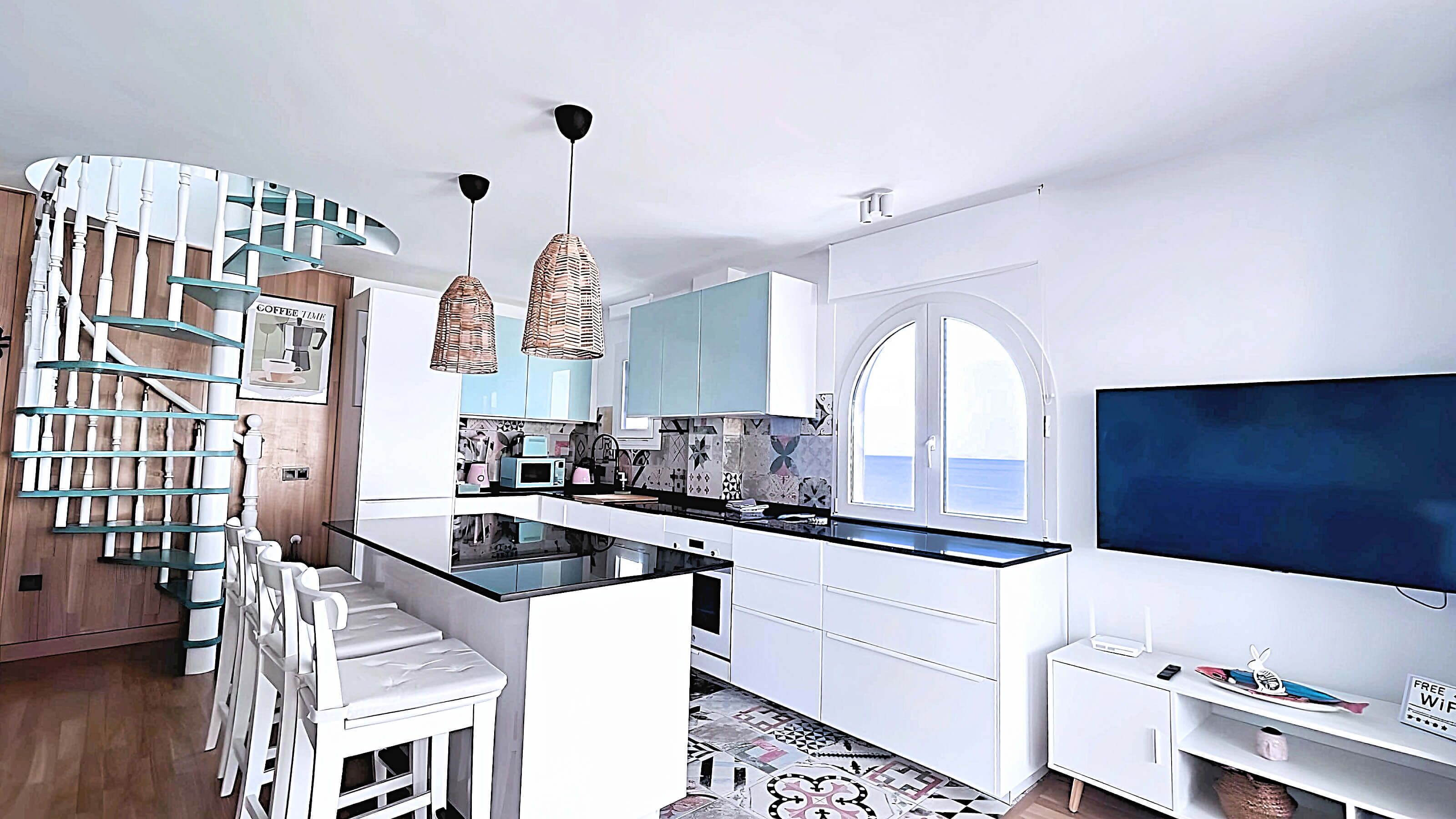 A modern kitchen with white cabinetry, a central island, and a staircase with glass railings. - Albaida Gardens (El Morche)
