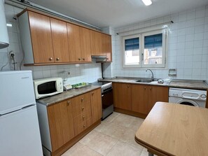 Ett kök med träskåp, en mikrovågsugn, en spis, ett handfat och en tvättmaskin.