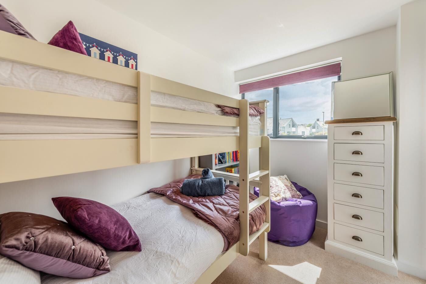 Une chambre avec un lit superposé, une fenêtre, une bibliothèque et une commode.