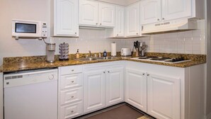 Una cocina con gabinetes blancos, un microondas, una cafetera y una estufa a gas.
