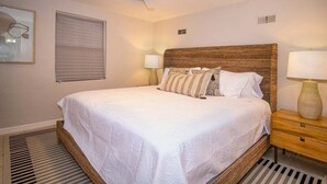 Un dormitorio ordenado con una cama grande, dos lámparas de noche, un ventilador de techo y una ventana con persianas.