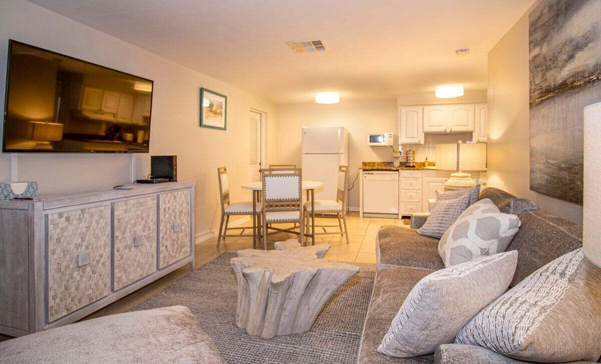 A compact living space with a sofa, a dining table with chairs, a kitchen area, and a flat-screen TV mounted on the wall.