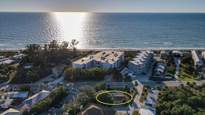 Vista aérea de una zona residencial costera con acceso a la playa, mostrando un conjunto de edificios de varios pisos con techos planos, un área de estacionamiento y un edificio destacado con una estructura de techo particular.
